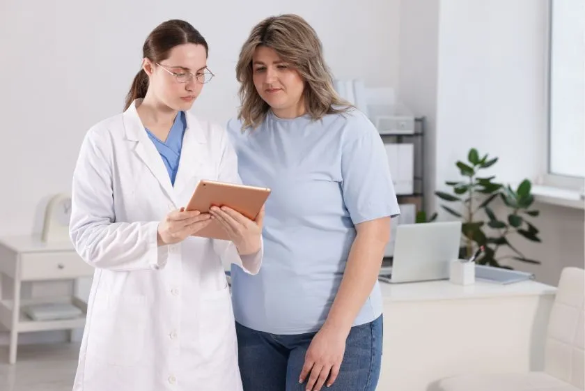 Lekarka w białym fartuchu omawia z pacjentką nowoczesne metody leczenia otyłości na tablecie w gabinecie medycznym.